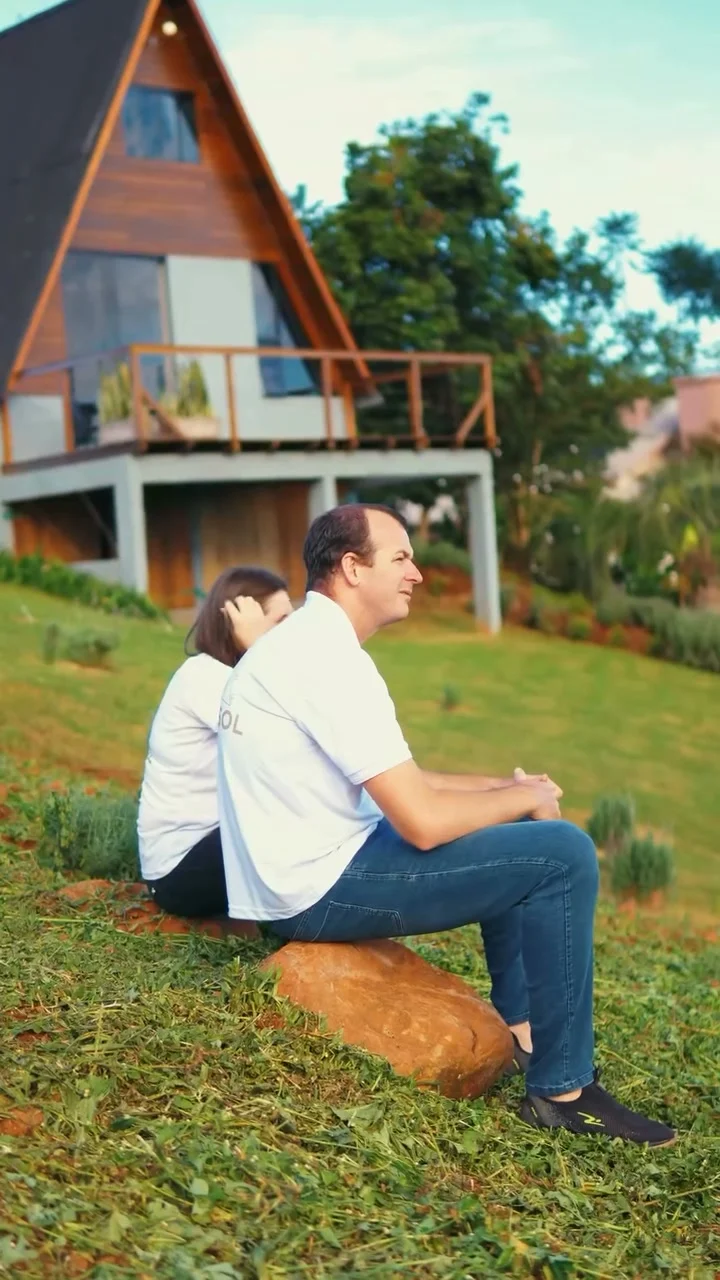 Eduardo e Juliane sentados no gramado diante do Chalé Girassol
